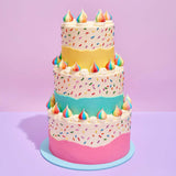 3 Tier Sprinkle Birthday Cake with colorful sprinkles and rainbow dollops on pastel yellow, blue, and pink layers by Crumbs & Doilies.